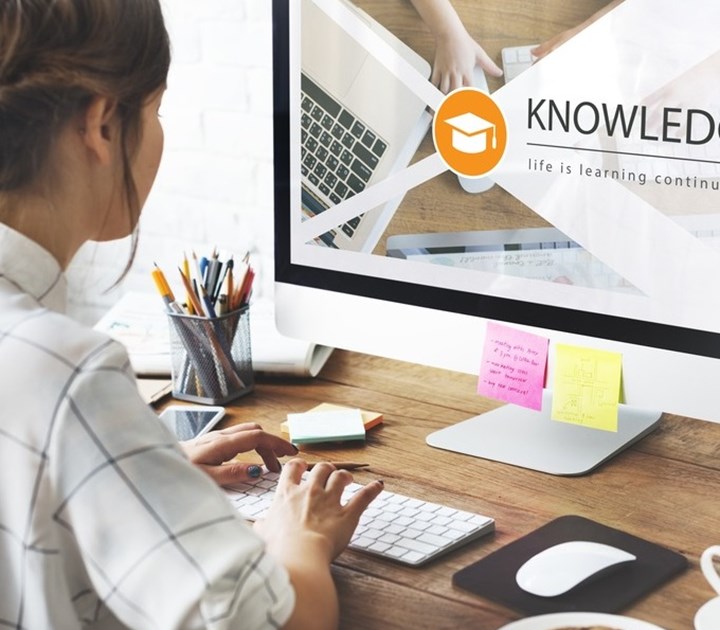 A person uses a computer displaying a learning website with the word KNOWLEDGE and a graduation cap icon. A keyboard, mouse, sticky notes, and pens are on the desk. The screen shows part of a laptop keyboard and text life is learning contin...