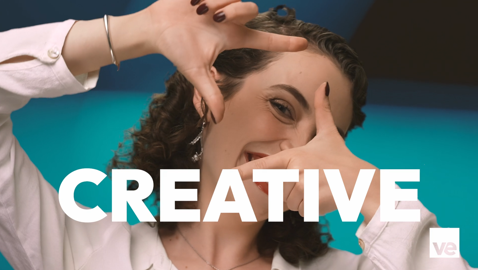 A person with curly hair and dark nail polish frames their face with their hands, forming a rectangle. They wear a white shirt and silver jewelry. The background is teal, and the word CREATIVE is bold and centered in white text.