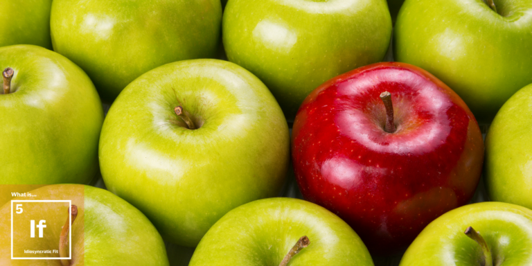 A group of green apples with one red apple in the center. The green apples surround the red apple, highlighting its color contrast. In the bottom left corner, theres text on a transparent square.